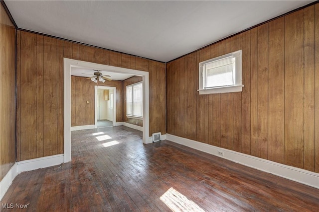 unfurnished room with hardwood / wood-style flooring, baseboards, a ceiling fan, and wooden walls