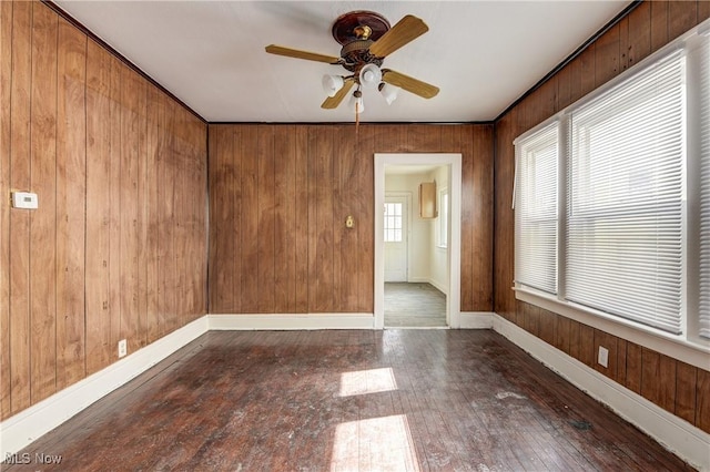 spare room with ceiling fan, baseboards, wood walls, and wood finished floors
