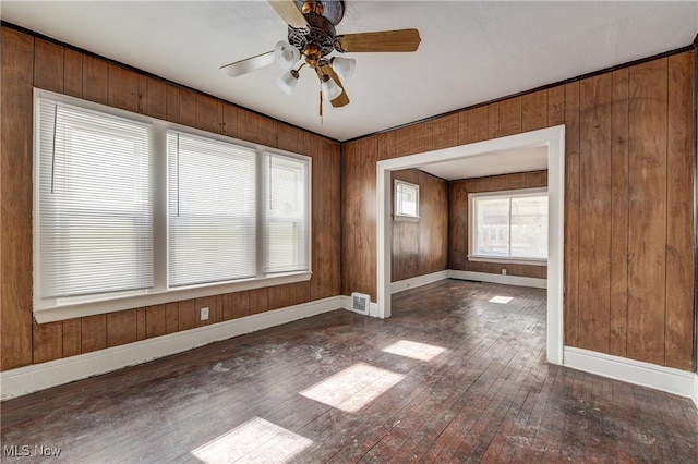 unfurnished room with hardwood / wood-style flooring, a ceiling fan, baseboards, and wooden walls