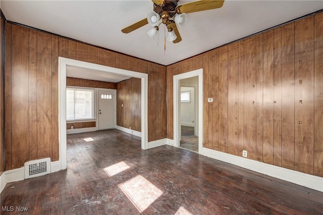unfurnished room featuring ceiling fan, hardwood / wood-style floors, baseboards, and wooden walls