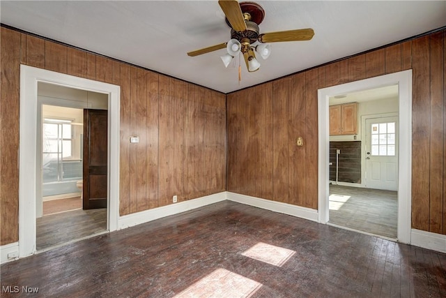empty room with healthy amount of natural light, hardwood / wood-style floors, ceiling fan, wood walls, and baseboards