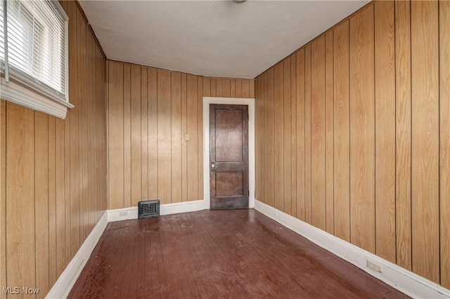 empty room featuring wood-type flooring, wooden walls, and baseboards