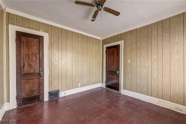 unfurnished room featuring ceiling fan, wood walls, baseboards, and wood finished floors