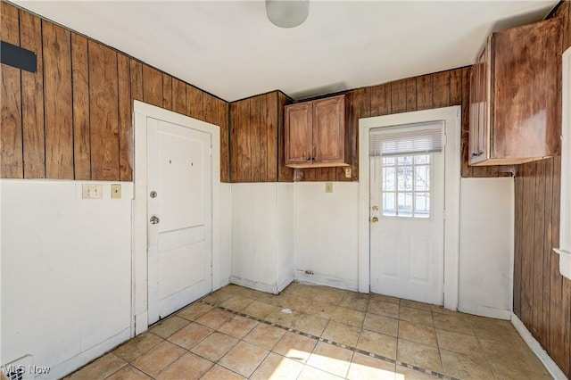 doorway with light tile patterned flooring and wood walls