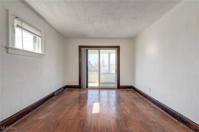 unfurnished room featuring plenty of natural light, hardwood / wood-style flooring, a textured ceiling, and baseboards