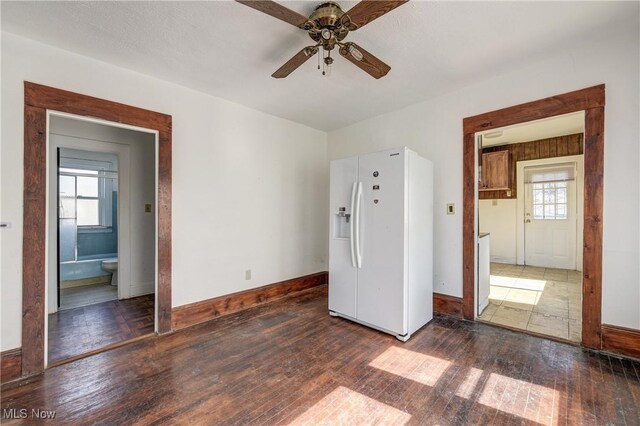 unfurnished bedroom with white fridge with ice dispenser, baseboards, and multiple windows