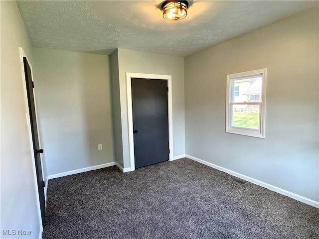 1226 E Main St, Coshocton, OH 43812 - unfurnished bedroom with dark carpet, a textured ceiling, baseboards, and a closet