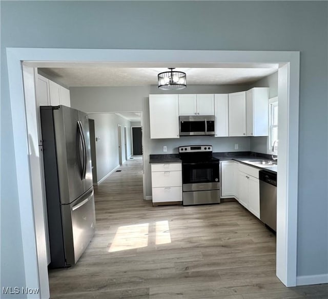 1226 E Main St, Coshocton, OH 43812 - kitchen featuring appliances with stainless steel finishes, a sink, dark countertops, light wood-style floors, and white cabinetry