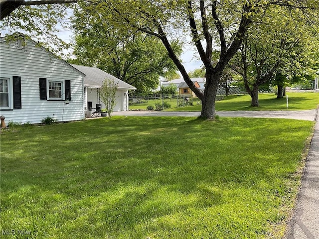 view of green lawn featuring an attached garage and asphalt driveway