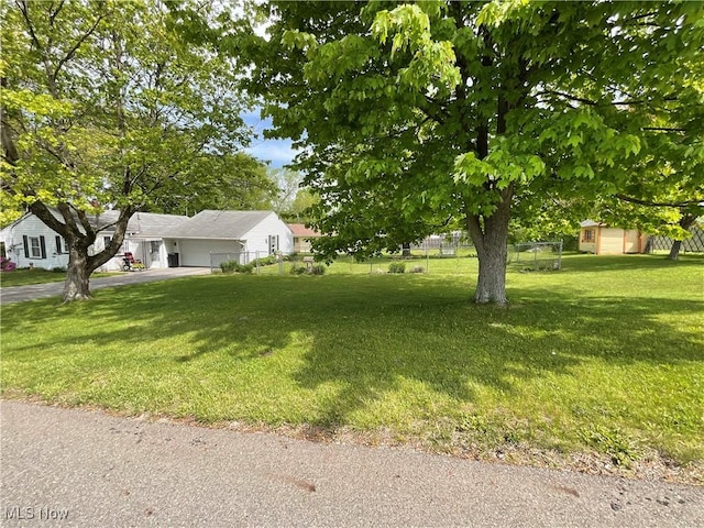view of yard featuring asphalt driveway, an attached garage, an outbuilding, and a storage unit
