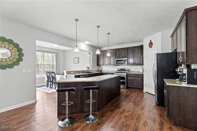 kitchen featuring stainless steel appliances, dark brown cabinetry, a kitchen bar, dark wood finished floors, and baseboards