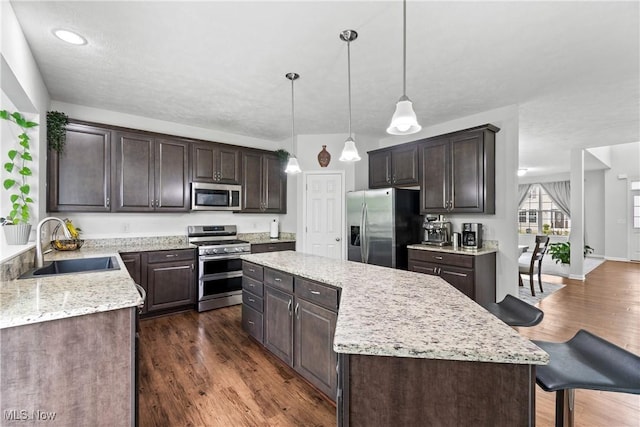 kitchen with stainless steel appliances, a sink, a kitchen island, and dark brown cabinets