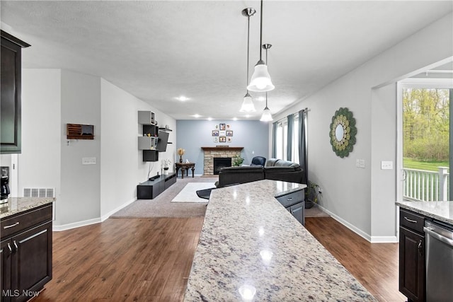kitchen featuring a stone fireplace, stainless steel dishwasher, dark wood-type flooring, baseboards, and light stone counters
