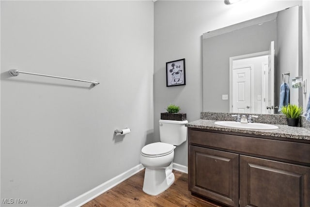 half bath featuring baseboards, toilet, wood finished floors, and vanity