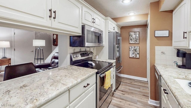 kitchen with appliances with stainless steel finishes, baseboards, light wood-type flooring, white cabinetry, and tasteful backsplash