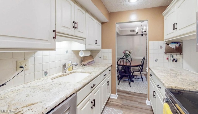 kitchen with a sink, light wood-style flooring, a chandelier, white cabinetry, and light stone countertops