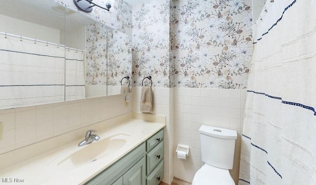 bathroom featuring wallpapered walls, tile walls, vanity, and toilet