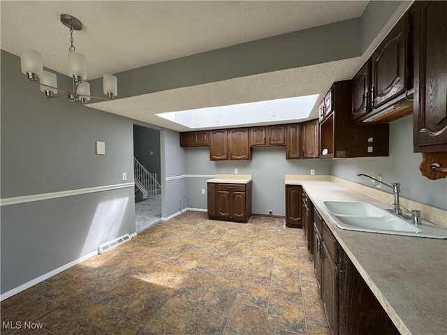 kitchen featuring a sink, dark brown cabinets, a skylight, baseboards, and a textured ceiling