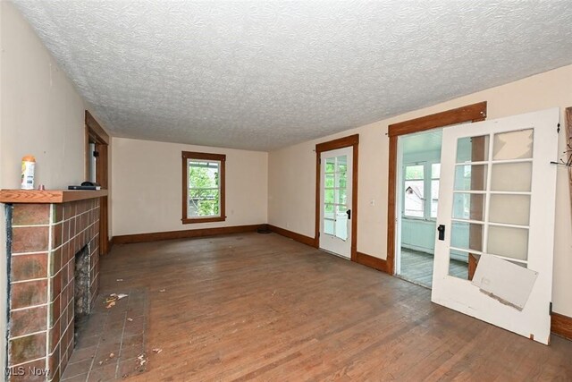 1324-1326 Shorb Ave NW, Canton, OH 44703 - unfurnished living room with wood finished floors, a brick fireplace, a textured ceiling, baseboards, and french doors