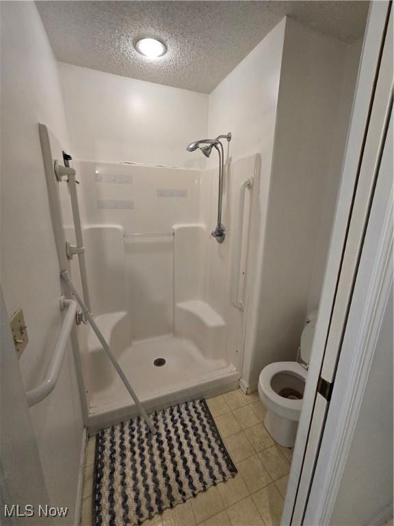 full bath featuring a textured ceiling, a shower stall, tile patterned floors, and toilet