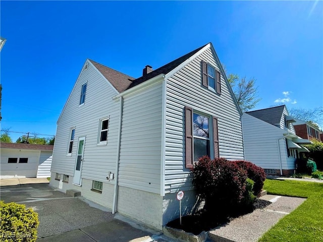 view of property exterior with an outbuilding, a chimney, roof with shingles, driveway, and a garage