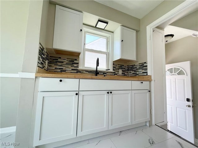 kitchen with wooden counters, white cabinetry, a sink, light marble finish floors, and decorative backsplash