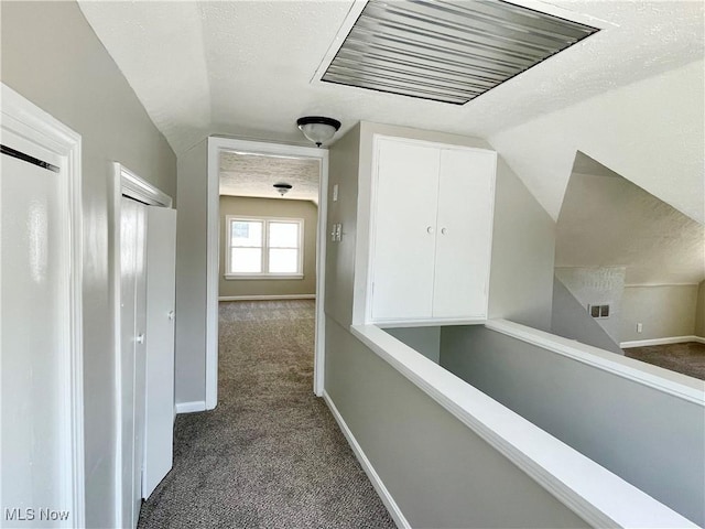 hallway featuring lofted ceiling, dark carpet, baseboards, a textured ceiling, and an upstairs landing