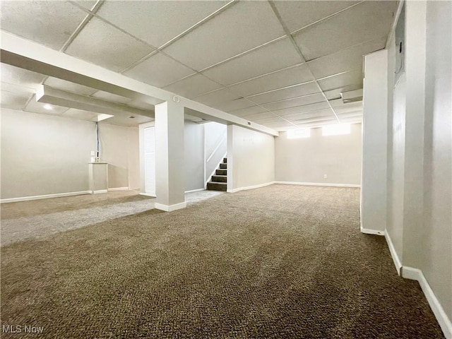 basement featuring a paneled ceiling, carpet flooring, stairs, and baseboards