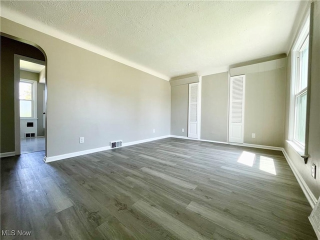 unfurnished bedroom featuring arched walkways, dark wood-type flooring, a textured ceiling, baseboards, and two closets