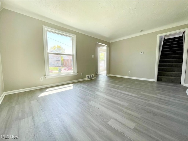 unfurnished living room with arched walkways, wood finished floors, baseboards, a textured ceiling, and stairway