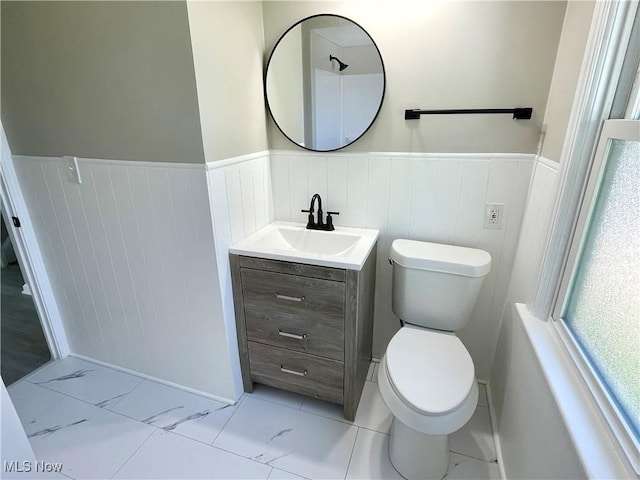 bathroom with a wainscoted wall, vanity, toilet, and marble look tiles