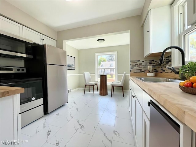 kitchen featuring appliances with stainless steel finishes, a sink, wood counters, light marble finish flooring, and white cabinets