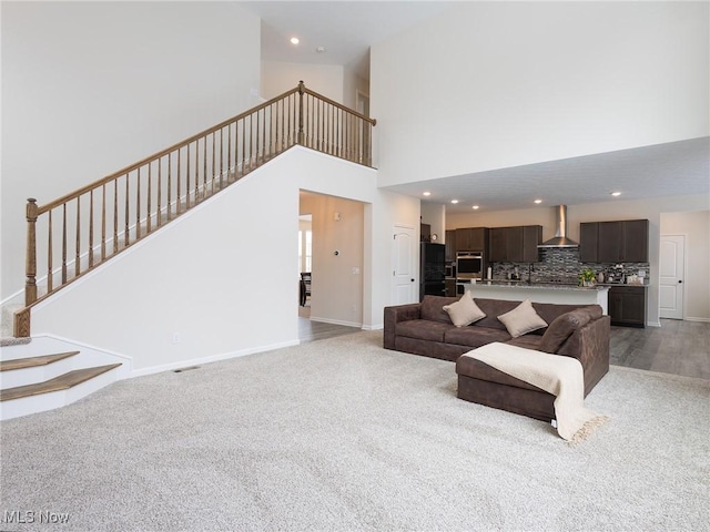 living area featuring stairway, baseboards, a high ceiling, recessed lighting, and light carpet