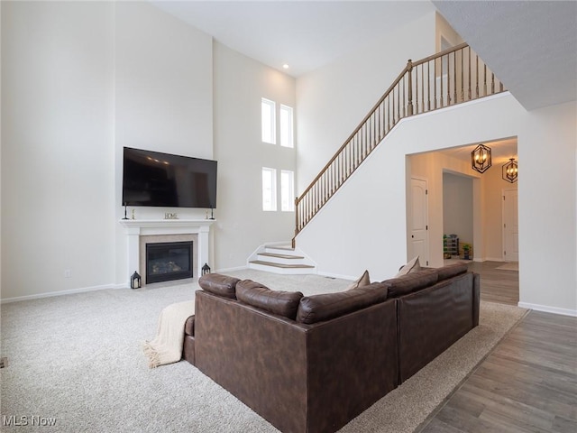 living room featuring a towering ceiling, baseboards, stairway, a fireplace with flush hearth, and a chandelier