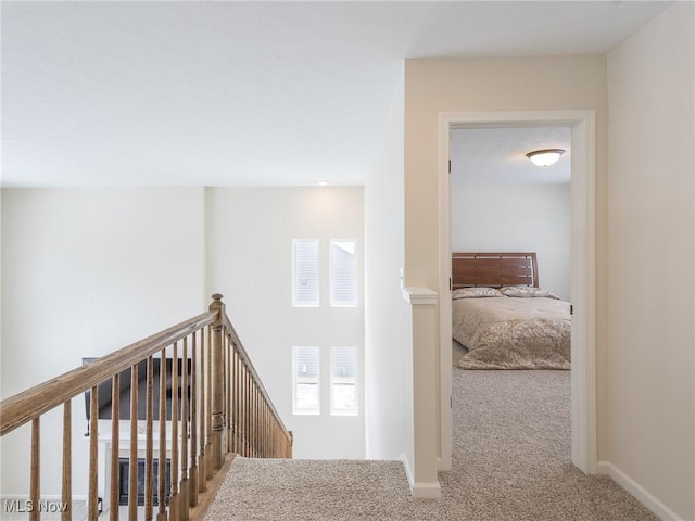 hallway featuring carpet flooring, an upstairs landing, and baseboards