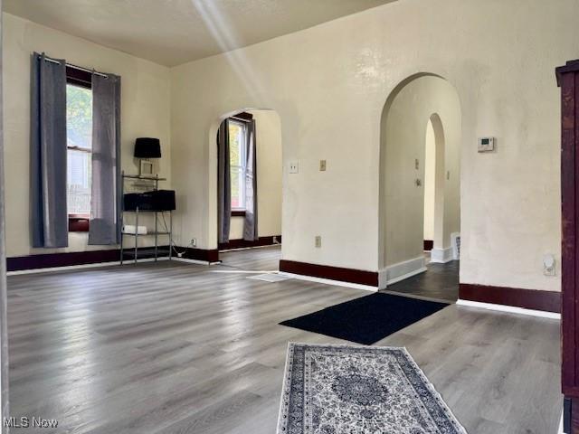 empty room with arched walkways, wood finished floors, and baseboards