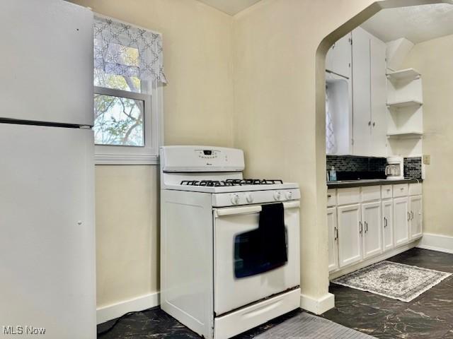 kitchen featuring white appliances, baseboards, open shelves, dark countertops, and white cabinetry