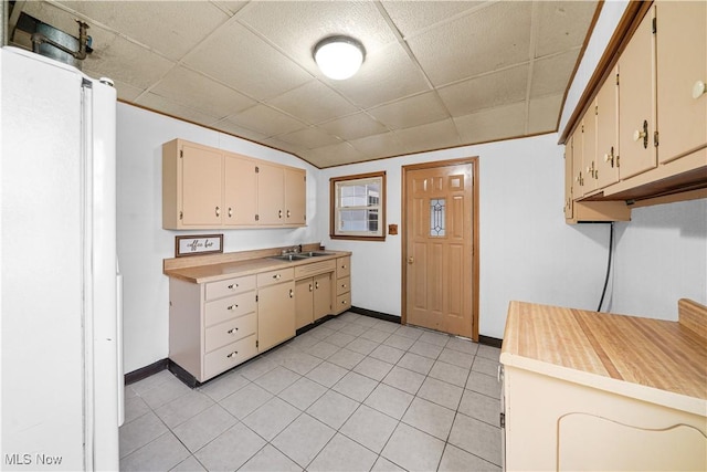 kitchen featuring baseboards, light countertops, a sink, and cream cabinetry