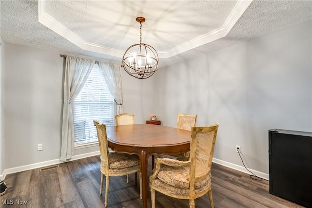 dining room featuring a textured ceiling, a chandelier, a raised ceiling, crown molding, and wood finished floors