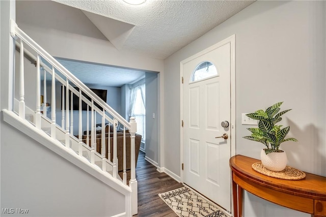 entrance foyer featuring dark wood-style flooring, a textured ceiling, stairway, and baseboards