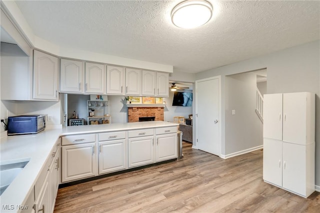 kitchen featuring ceiling fan, a textured ceiling, light countertops, light wood-style flooring, and a brick fireplace