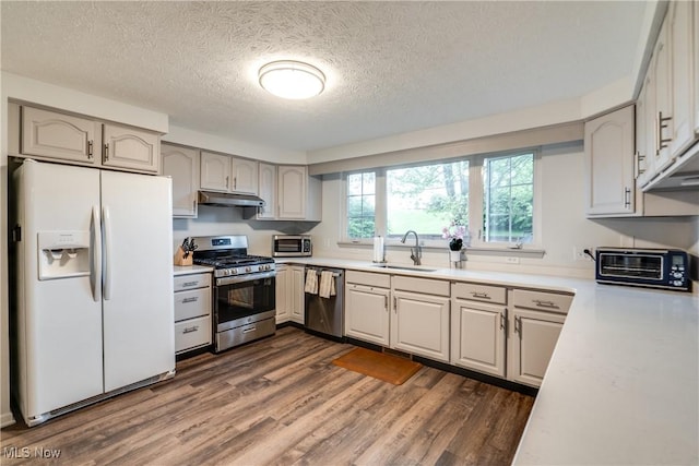 kitchen featuring stainless steel appliances, under cabinet range hood, dark wood-style flooring, a sink, and a textured ceiling