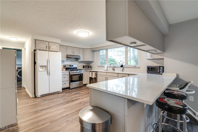 kitchen featuring appliances with stainless steel finishes, a peninsula, a sink, under cabinet range hood, and a kitchen breakfast bar