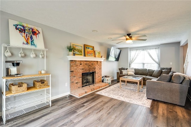 living room with ceiling fan, wood finished floors, a brick fireplace, and baseboards