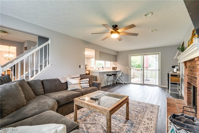 living room featuring wood finished floors, a fireplace, ceiling fan, stairs, and a textured ceiling