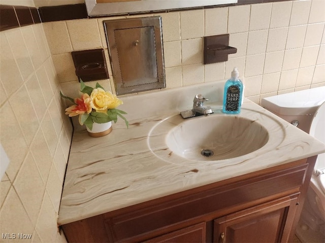 bathroom view of vanity, tile walls, toilet, and tasteful backsplash