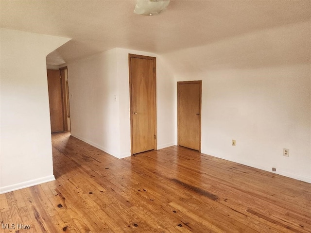 unfurnished room with wood finished floors, baseboards, arched walkways, and lofted ceiling