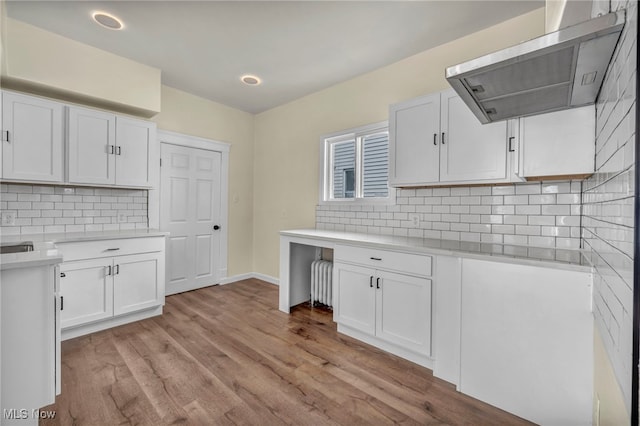 kitchen featuring exhaust hood, white cabinetry, backsplash, and light wood finished floors