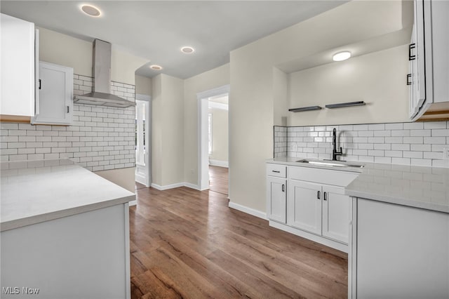 kitchen with wall chimney range hood, a sink, tasteful backsplash, and white cabinetry
