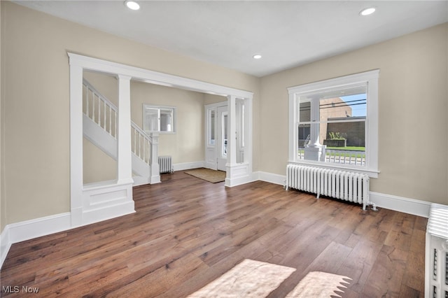 unfurnished living room featuring radiator heating unit, wood finished floors, baseboards, recessed lighting, and stairs